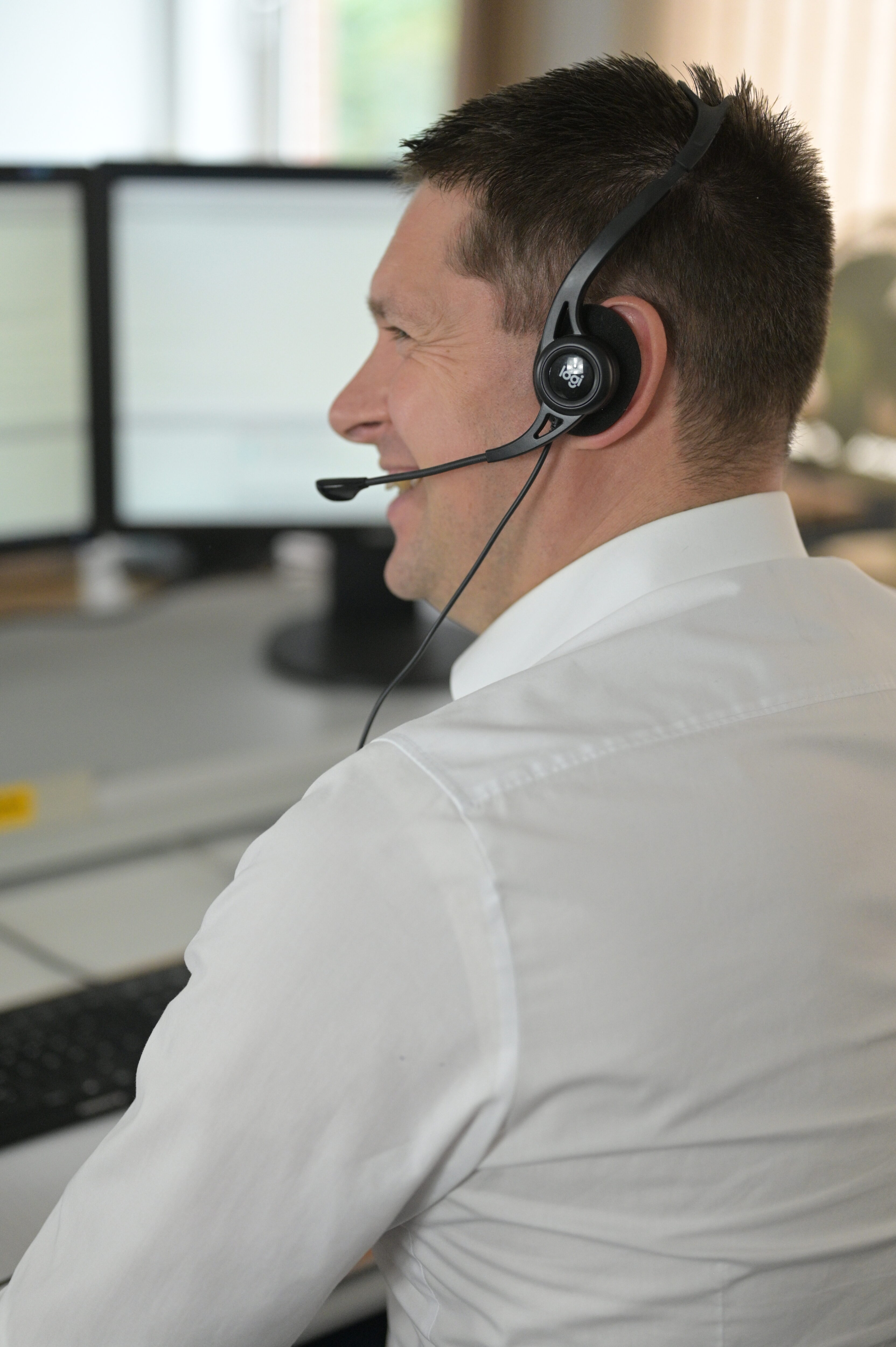 Ein lachender Servicemitarbeiter an einem Bürotisch. Er trägt ein Headset.