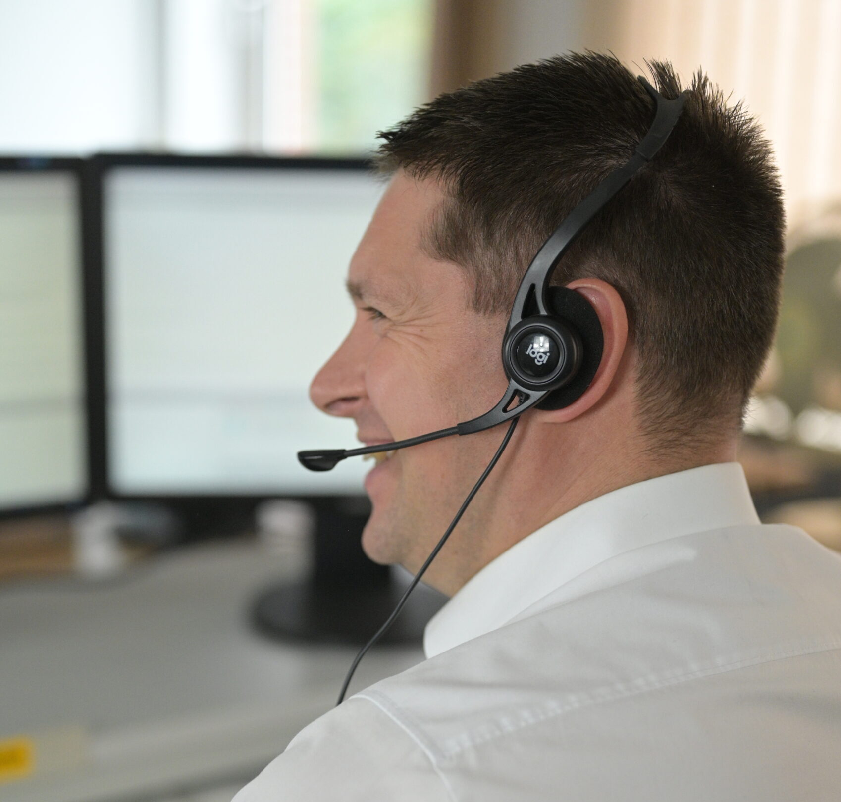 Ein lachender Servicemitarbeiter an einem Bürotisch. Er trägt ein Headset.